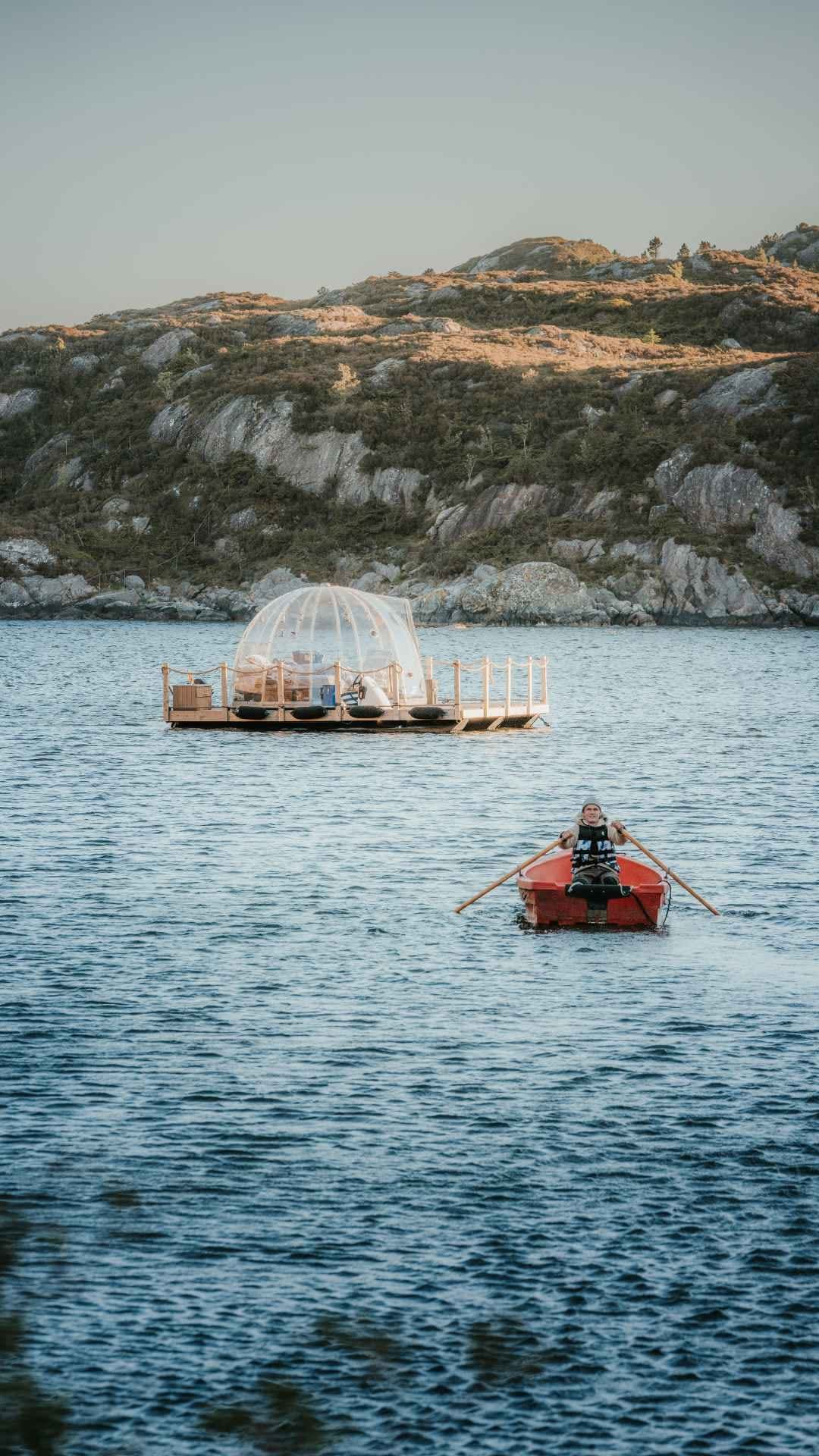 Annonse: en glassdome på en flåte ute i en fjord, med en person som ror en rød robåt bortover mot den.